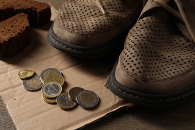 Poverty. Old shoes, coins, pieces of bread and cardboard sheet on wooden table, closeup