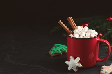 Photo of Delicious hot chocolate with marshmallows, cinnamon and gingerbread cookies on black table, space for text