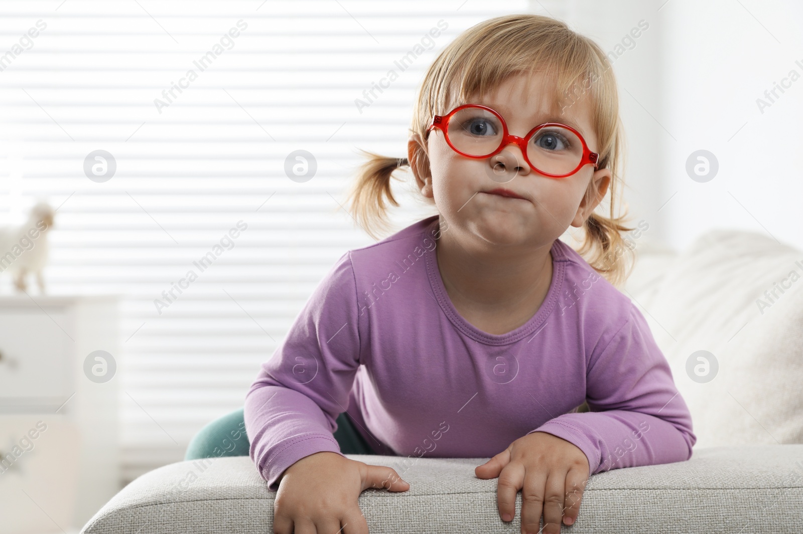 Photo of Cute little girl in glasses on sofa at home. Space for text