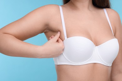 Photo of Mammology. Woman in bra doing breast self-examination on light blue background, closeup