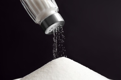 Photo of Pouring salt from shaker on black background, closeup