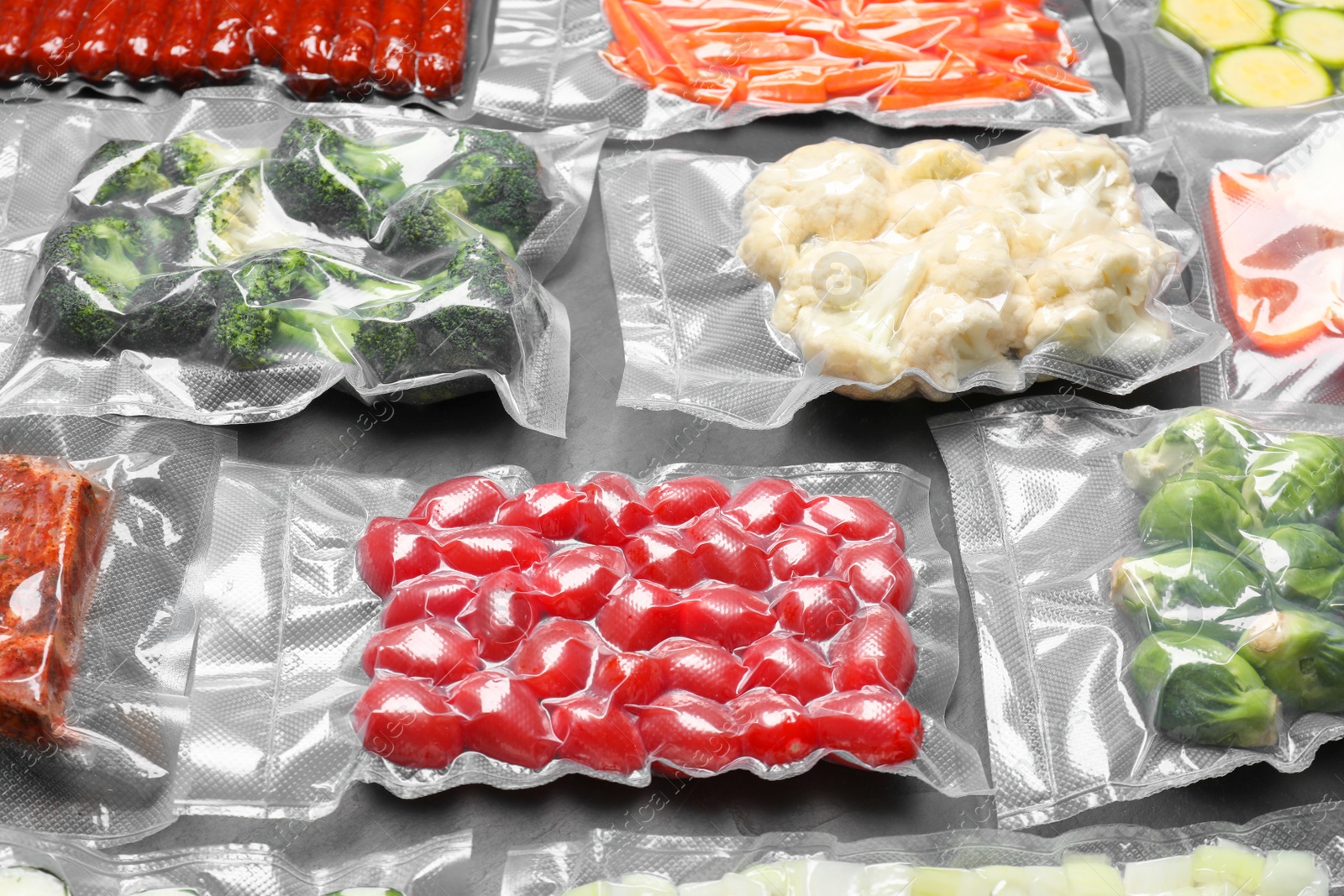 Photo of Many different food in vacuum packings on dark grey table, closeup