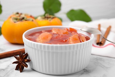 Photo of Bowl of tasty persimmon jam and ingredients on white marble table