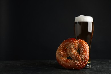 Photo of Tasty pretzel and glass of beer on black table against dark background, space for text