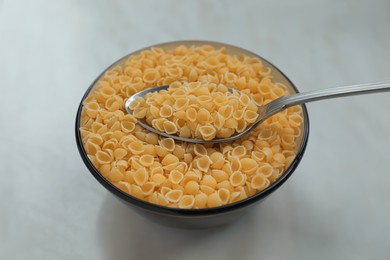 Bowl of uncooked conchiglie pasta and spoon on white marble table, closeup