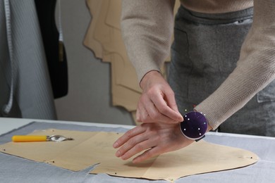 Photo of Tailor pinning sewing pattern to fabric at table in atelier, closeup