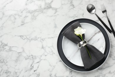 Photo of Stylish setting with cutlery, napkin, flowers and plates on white marble table, top view. Space for text