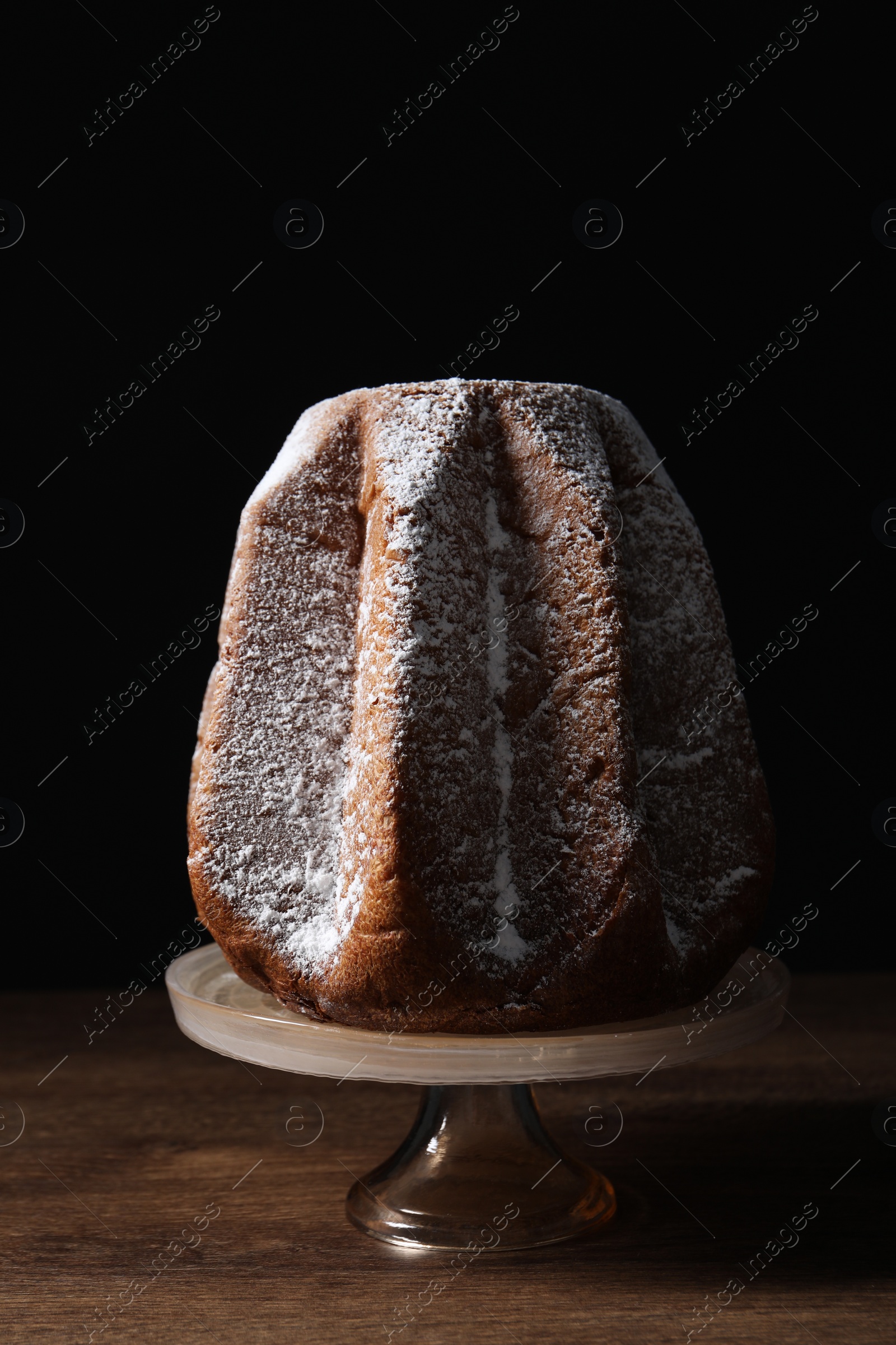Photo of Delicious Pandoro cake decorated with powdered sugar on wooden table. Traditional Italian pastry