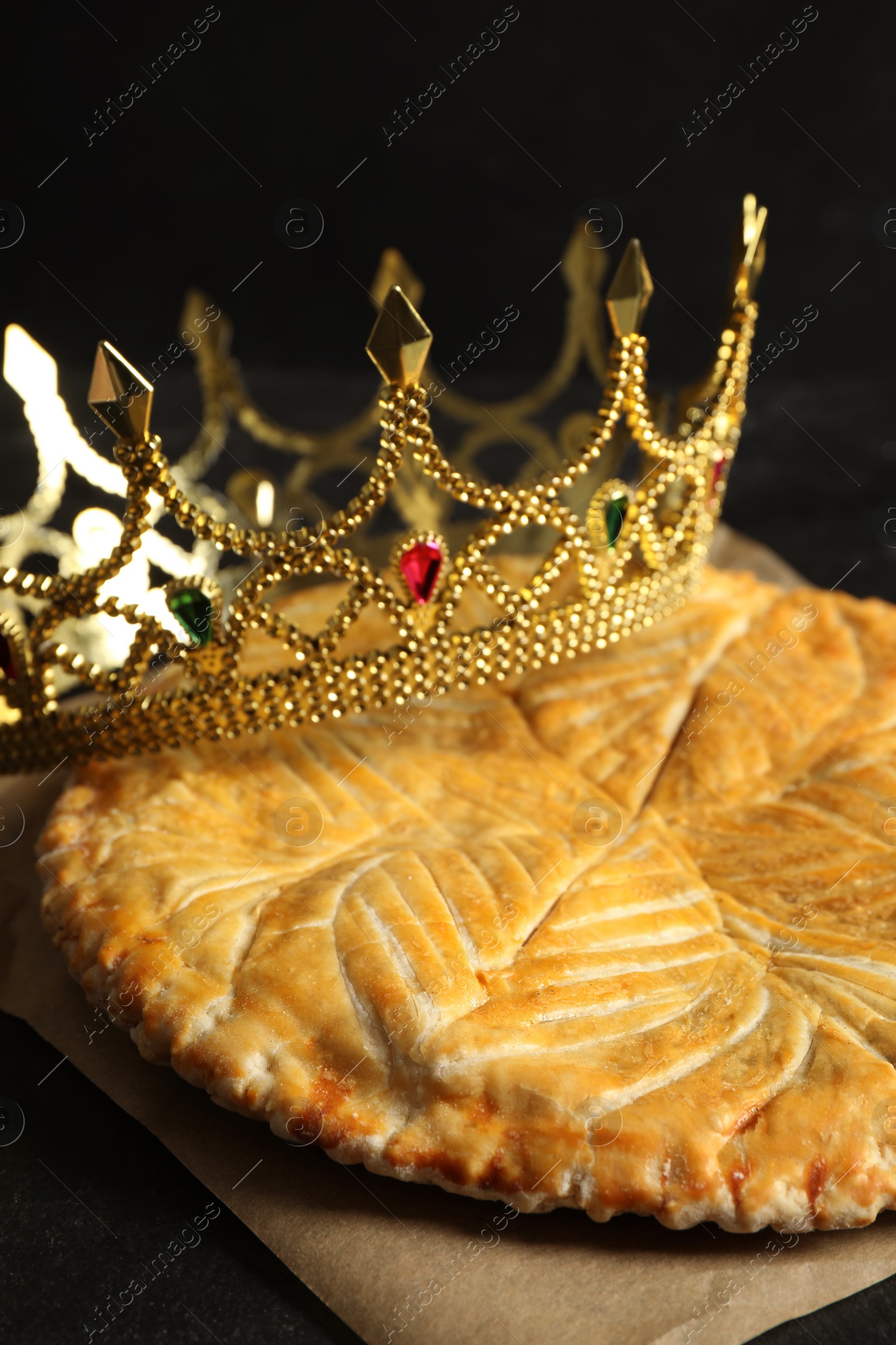 Photo of Traditional galette des Rois with decorative crown on black table, closeup