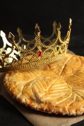 Photo of Traditional galette des Rois with decorative crown on black table, closeup