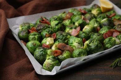 Photo of Delicious roasted Brussels sprouts and bacon in baking dish on wooden table, closeup