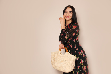 Young woman wearing floral print dress with straw bag on beige background. Space for text