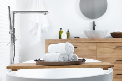 Photo of Rolled bath towels on tub tray in bathroom