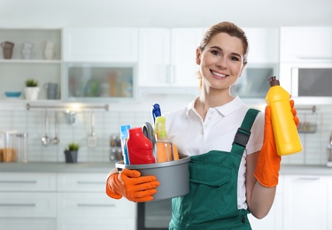 Photo of Portrait of young woman with basin of detergents and bottle in kitchen. Cleaning service