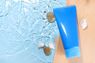 Tube of face cleansing product, stones and seashells on wooden table against light blue background, flat lay. Space for text