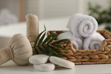 Photo of Spa composition. Towels, stones, herbal bags and palm leaves on white table indoors, closeup