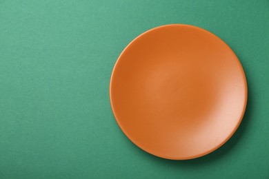 Photo of Empty orange ceramic plate on green background, top view. Space for text