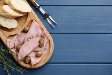 Photo of Slices of delicious ham with olives and baguette served on blue wooden table, flat lay. Space for text