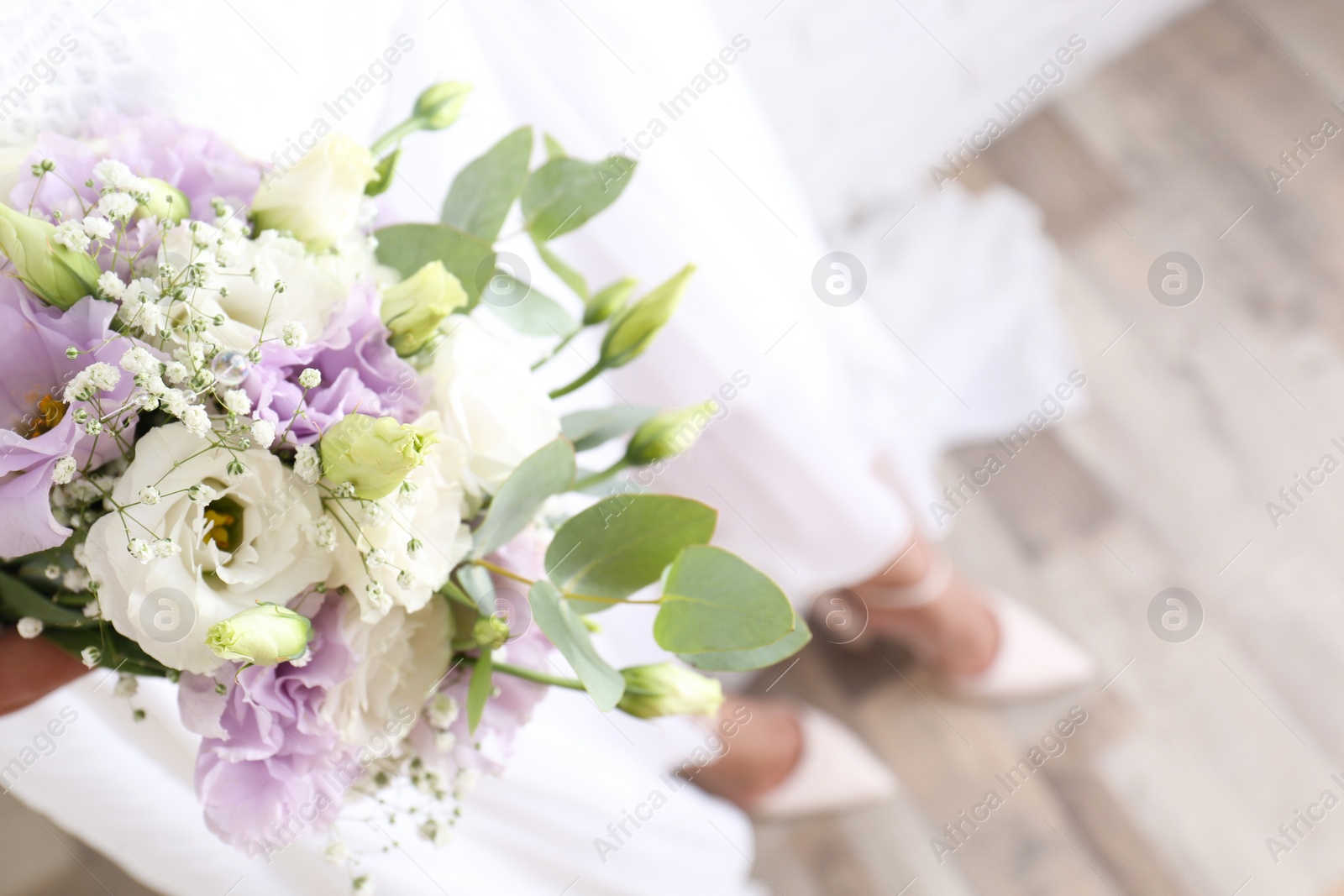 Photo of Bride holding beautiful bouquet with Eustoma flowers indoors, closeup