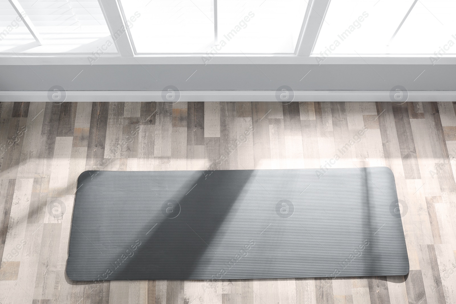 Photo of Unrolled grey yoga mat on floor in room, above view