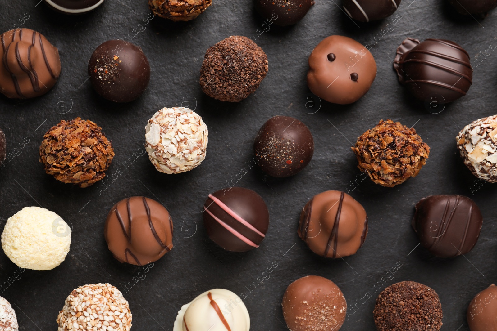 Photo of Different delicious chocolate candies on black table, flat lay