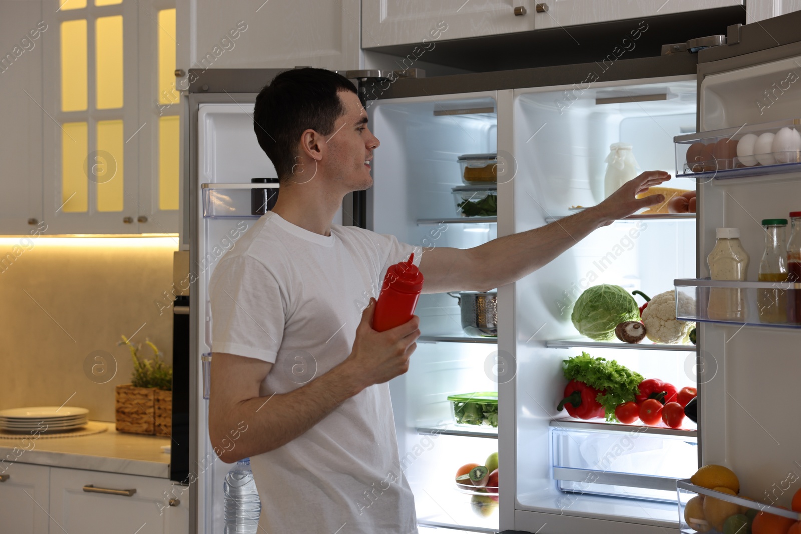 Photo of Man with ketchup near refrigerator in kitchen