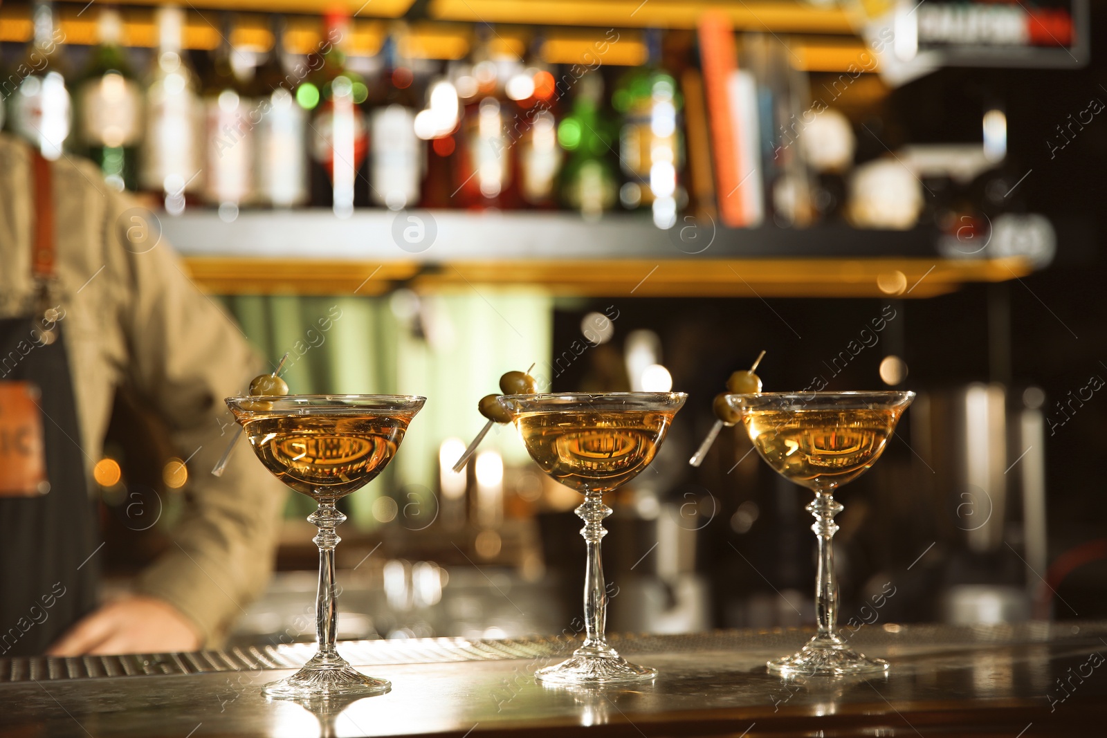 Photo of Glasses of martini cocktail with olives on bar counter. Space for text