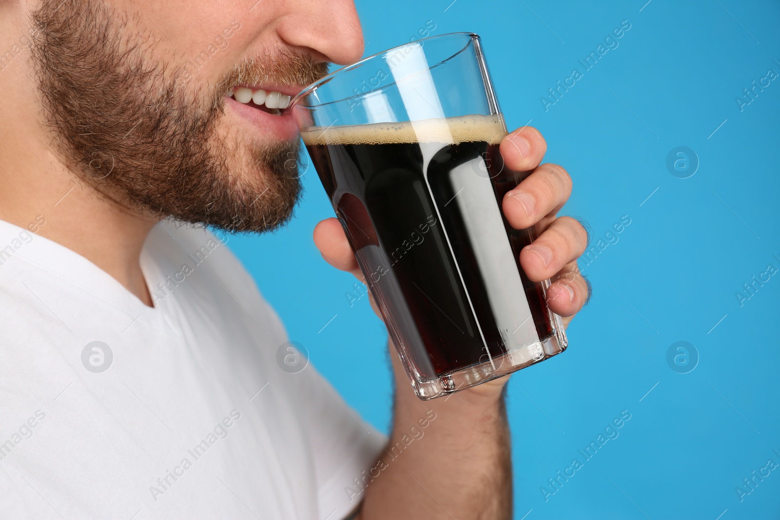 Photo of Young man with cold kvass on blue background, closeup. Traditional Russian summer drink