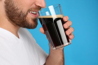 Young man with cold kvass on blue background, closeup. Traditional Russian summer drink