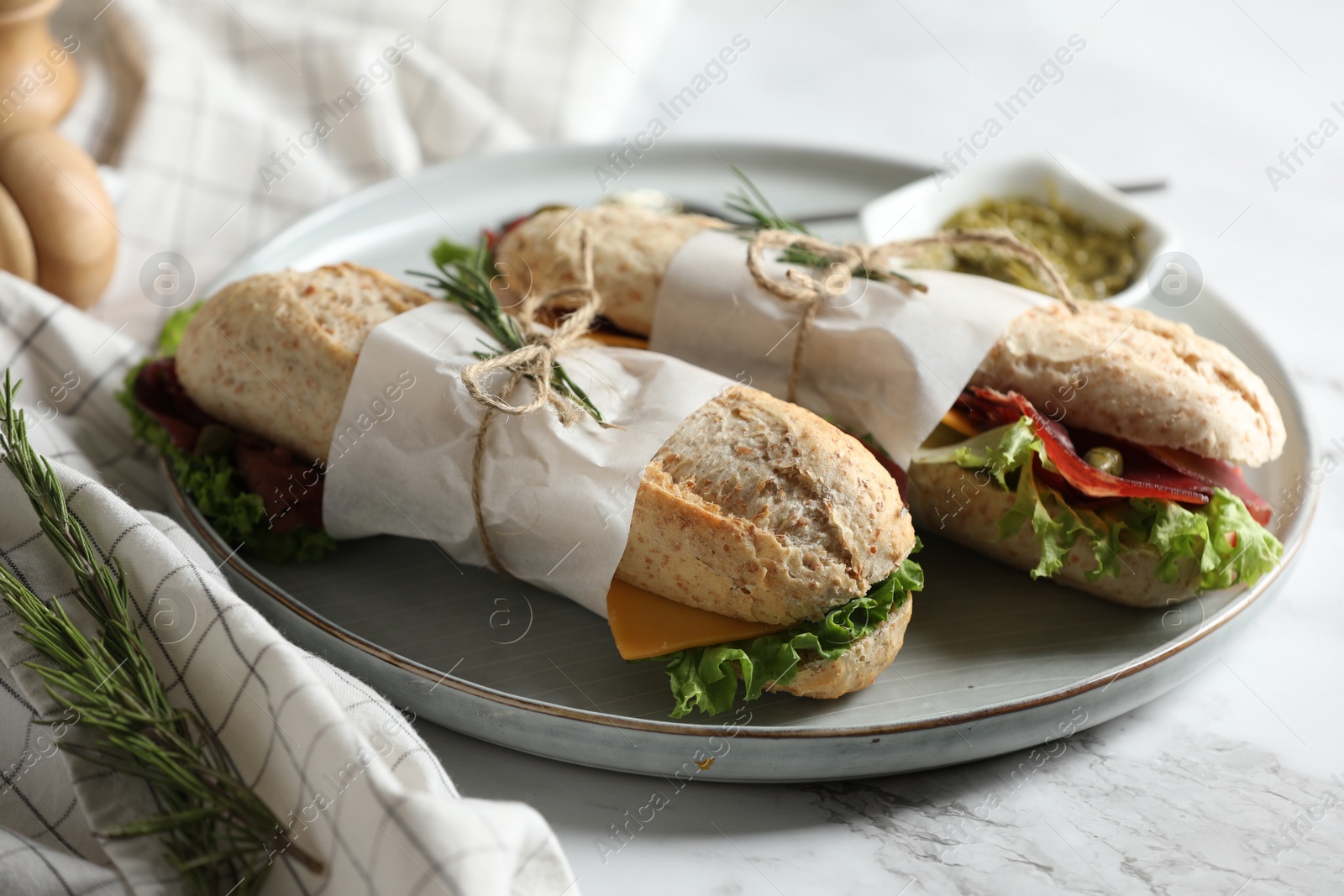 Photo of Delicious sandwiches with bresaola, lettuce and cheese on white marble table, closeup