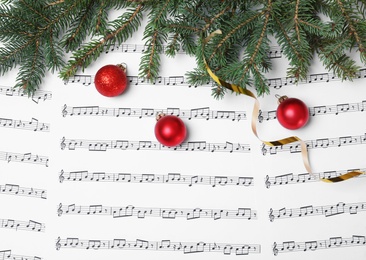 Composition with Christmas balls and fir tree branches on music sheets, top view