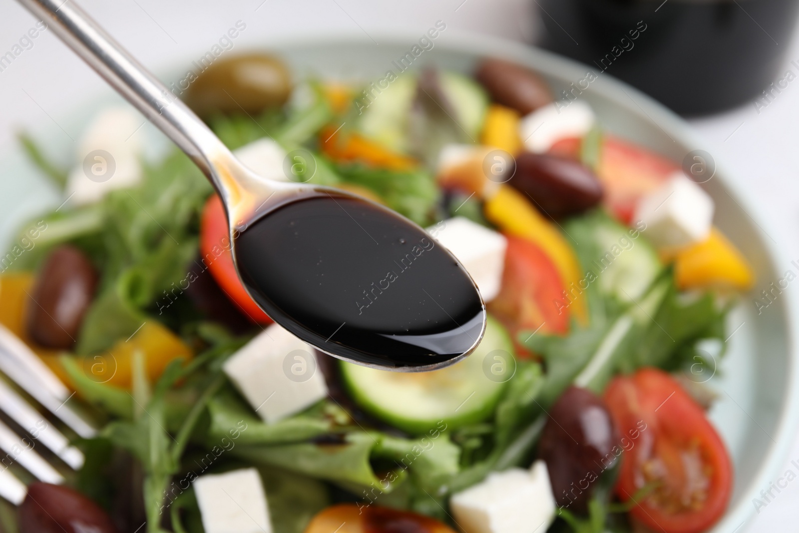 Photo of Pouring vinegar from spoon into plate with salad at table, closeup