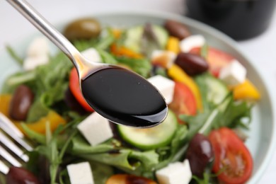 Pouring vinegar from spoon into plate with salad at table, closeup