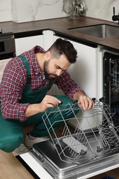 Photo of Serviceman examining dishwasher lower rack in kitchen