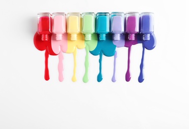 Spilled colorful nail polishes and bottles on white background, top view