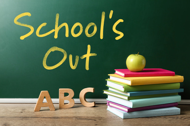 Image of Books, letters and apple on wooden table near chalkboard with text SCHOOL'S OUT