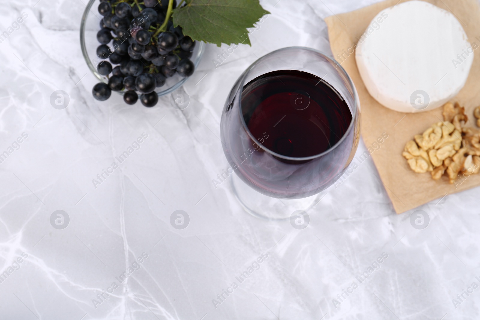 Photo of Glass of red wine and snacks served on white marble table, above view. Space for text