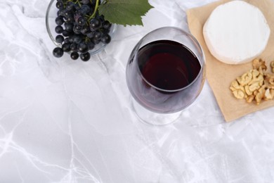 Photo of Glass of red wine and snacks served on white marble table, above view. Space for text