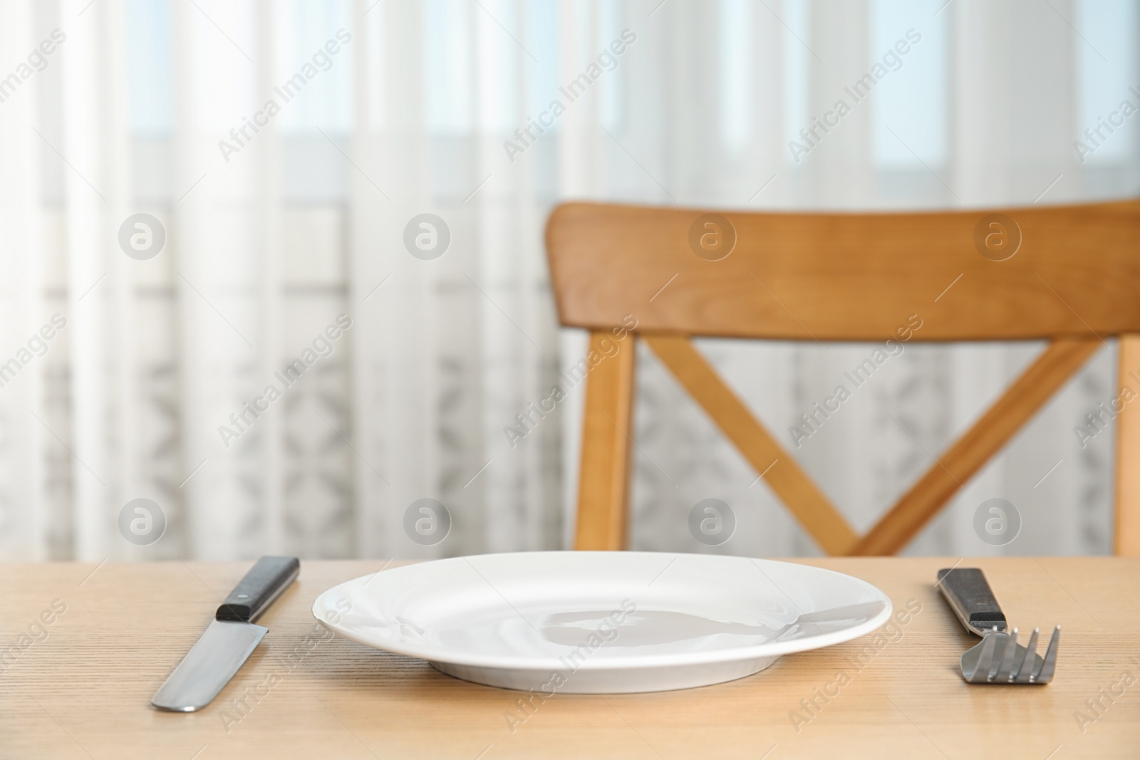 Photo of Empty white ceramic plate, fork and knife on wooden table