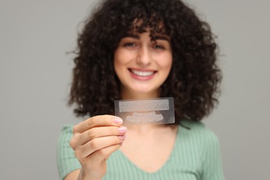 Photo of Young woman holding teeth whitening strips on grey background, selective focus