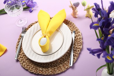 Photo of Festive table setting with painted egg, plates and iris flowers on lilac background. Easter celebration