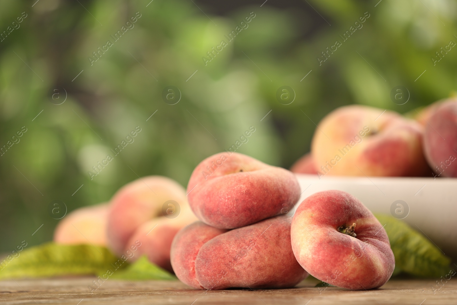 Photo of Fresh ripe donut peaches on wooden table against blurred green background. Space for text