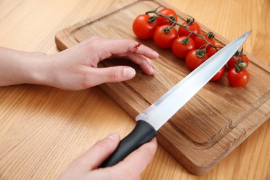 Photo of Woman cut finger with knife while cooking at wooden table, closeup