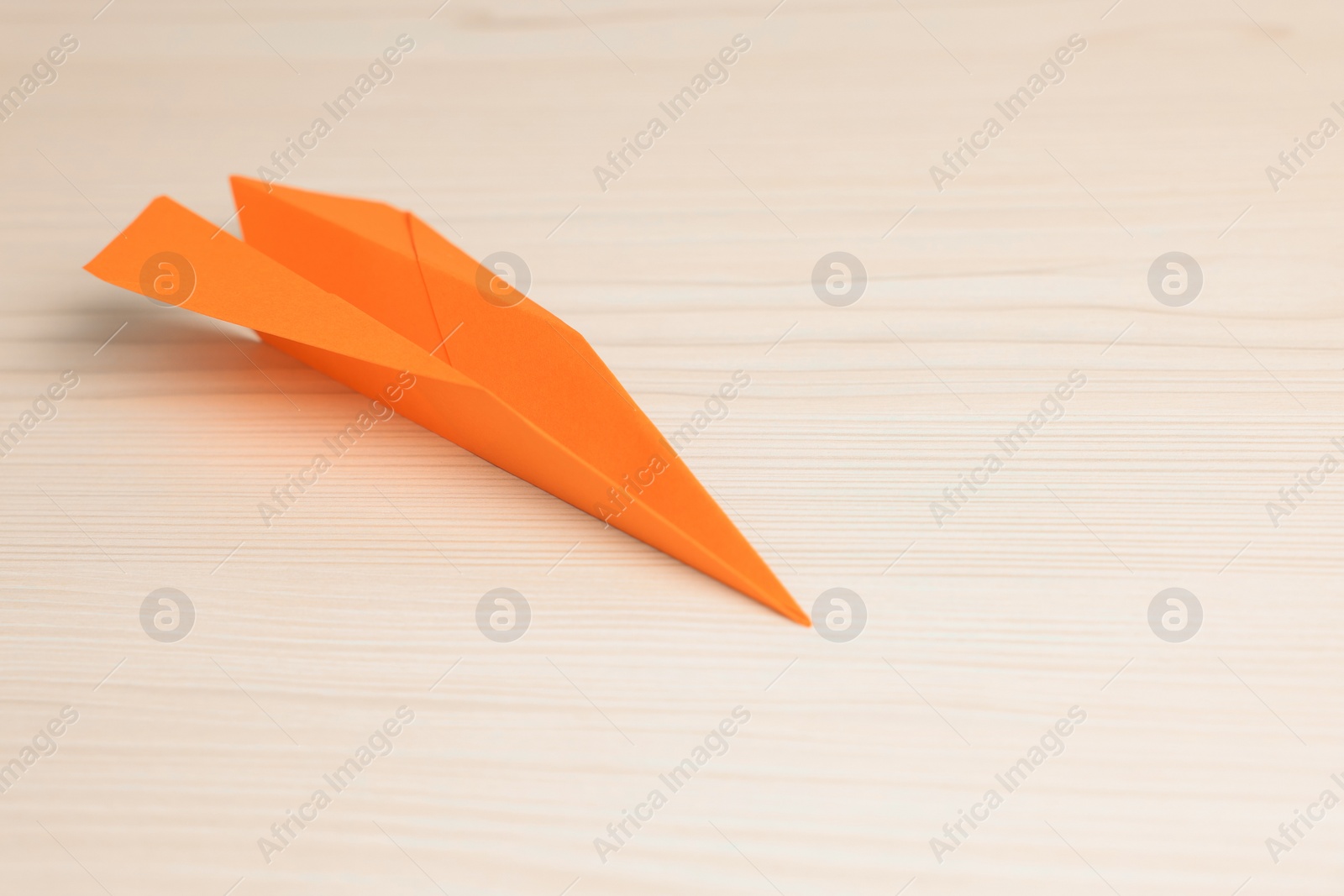 Photo of Handmade orange paper plane on beige wooden table. Space for text