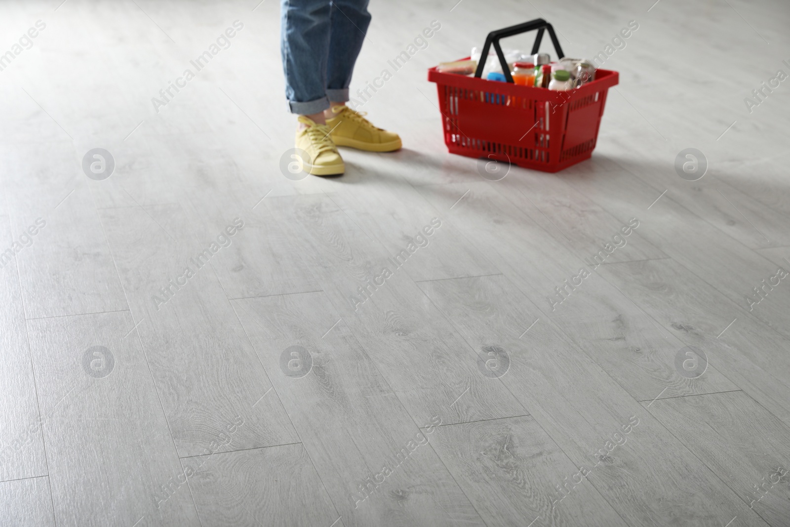 Photo of Woman and shopping basket with groceries on white wooden floor, closeup. Space for text