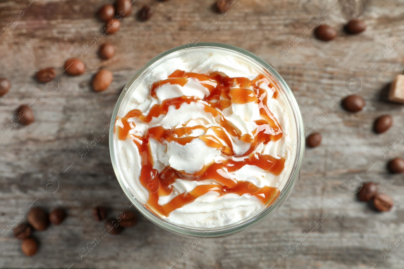 Photo of Glass of coffee with caramel topping on wooden background, top view