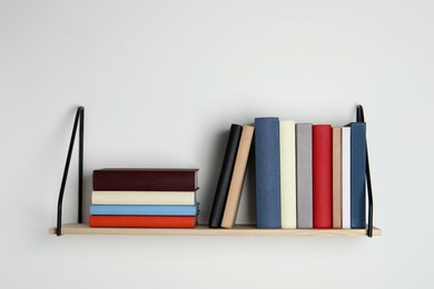 Wooden shelf with many hardcover books on white wall