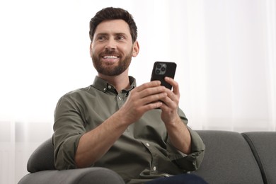 Photo of Smiling man using smartphone on sofa at home