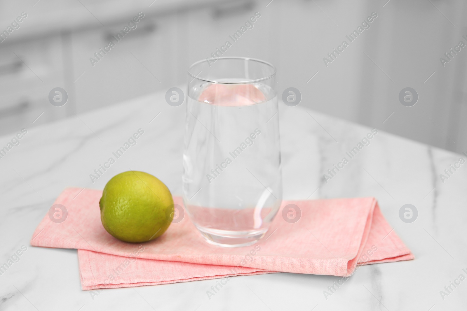 Photo of Filtered water in glass and lime on white marble table indoors, closeup