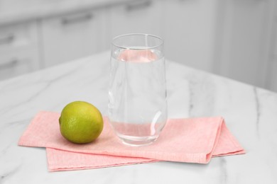 Photo of Filtered water in glass and lime on white marble table indoors, closeup